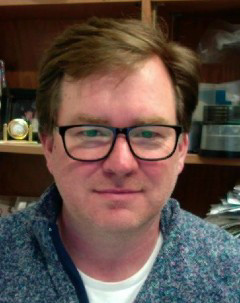 Headshot of Dr. Boraston with wooden shelves in background