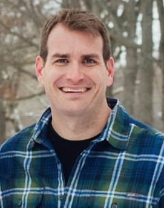 Smiling headshot of Dr. John Burke with a forested background.