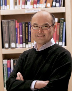 Smiling Dr. Lum with arms crossed in front of bookshelf