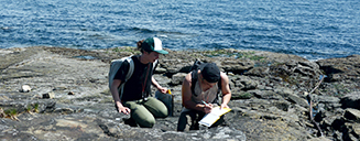 Two students writing in a notebook by the ocean