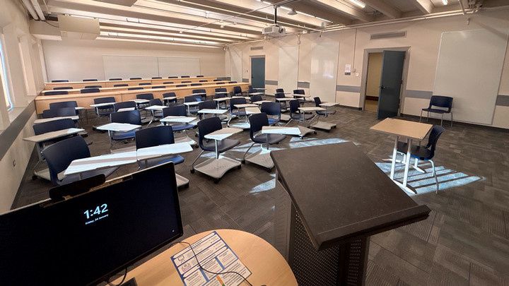 View from the presenter area featuring a desktop monitor, AV cabinet and podium facing the seating area.