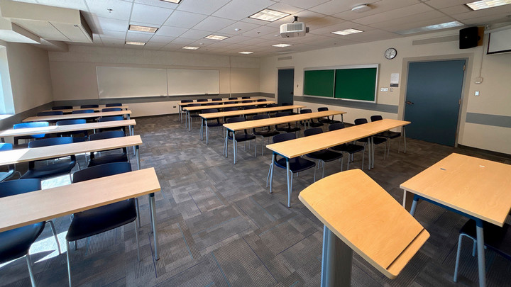 View from the presenter area with a podium and table with chair facing the seating area. The AV cabinet faces the wall instead of the class.