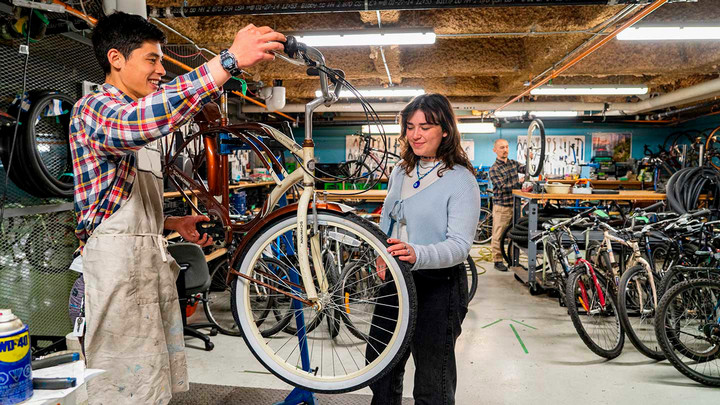 A BikeHub volunteer tests the pedals on on a vintage-style bicycle while a student tests the tire pressure.