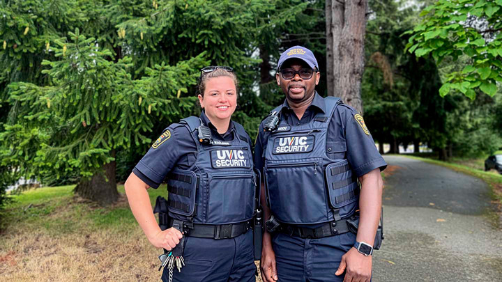 2 security officers wearing blue uniforms smile and pose outdoors