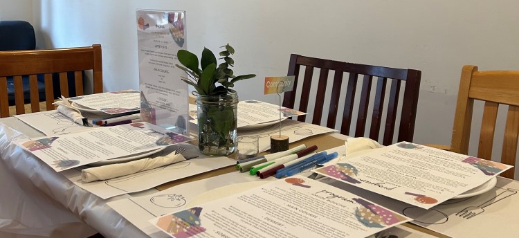 A view of a table setting before a Nourish+Flourish event. Printed programs, utensils, markers and eucalyptus in a mason jar.