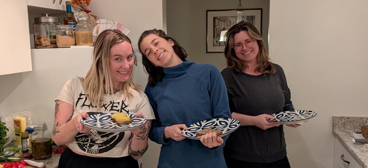Three students holding up meals in a home kitchen