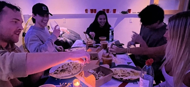 A group of students around a dinner table, smiling and eating