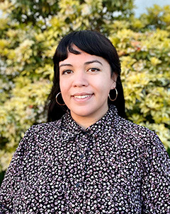 Photo of Megan Quigley from the shoulders up. She has long black hair with bangs and a floral top.