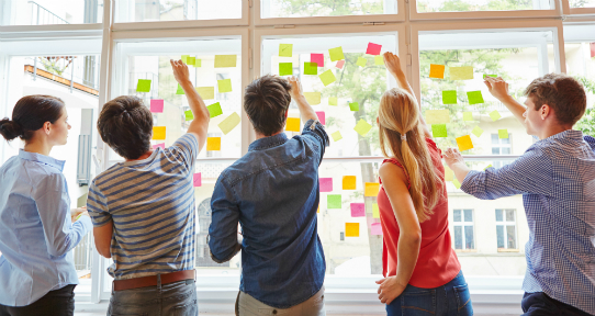 Students standing up and placing post-it notes on a window.