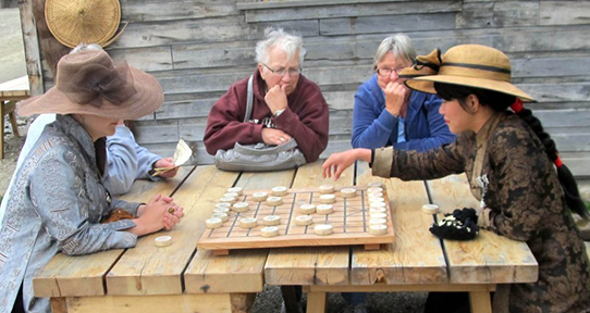 Student playing a board game in Barkerville with elderly tourists