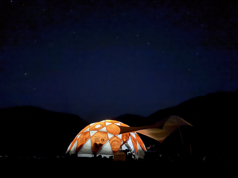 An orange tent alight on a dark stary night.