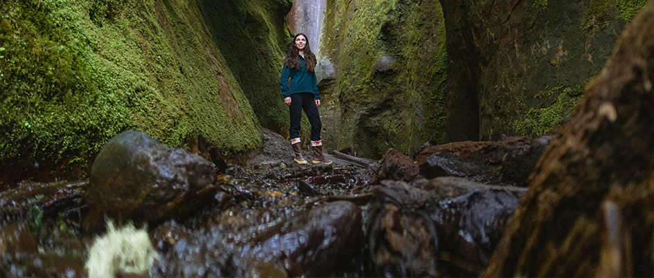 Student standing between moss covered rock walls in front of a small waterfall