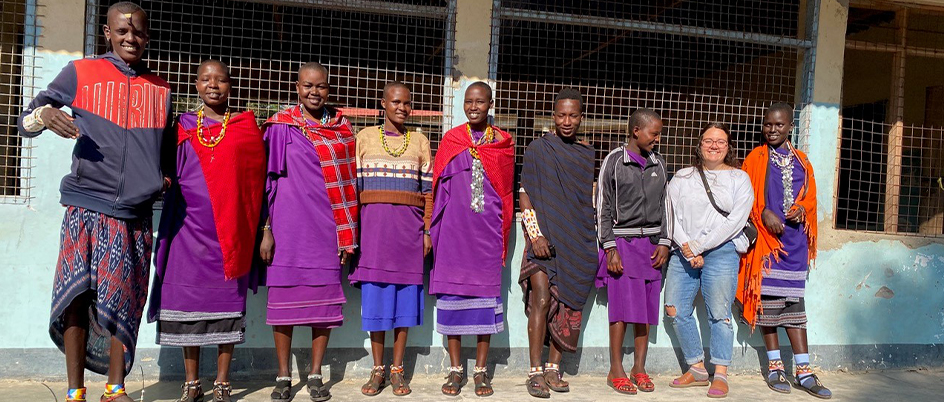 Student poses with Maasai youth in front of a stone wall