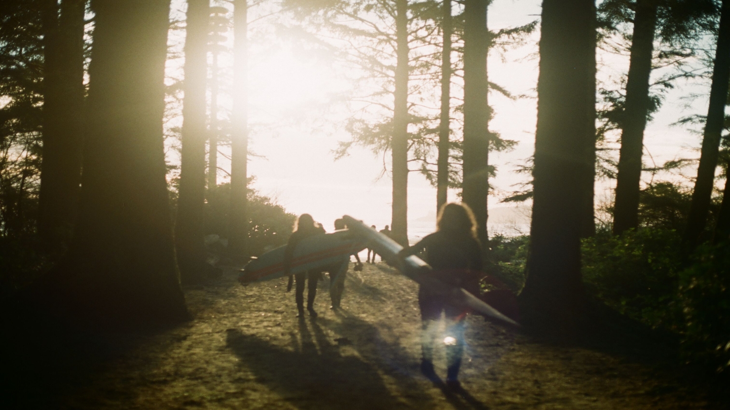 Students walking through forest towards beach with surfboards
