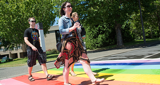 Three people walking across a rainbow coloured crosswalk at UVic