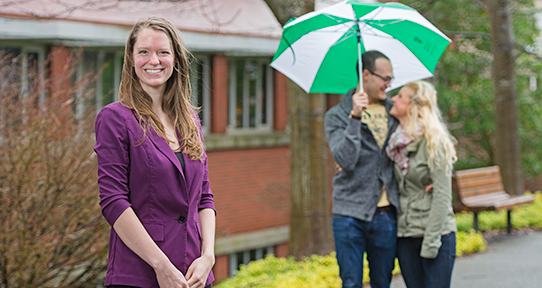PhD student on campus, with a couple in the background under an umbrella