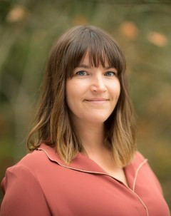 Imiage of Dr. Fischer in a pink top. The background is a slightly blurred out image of a forest.