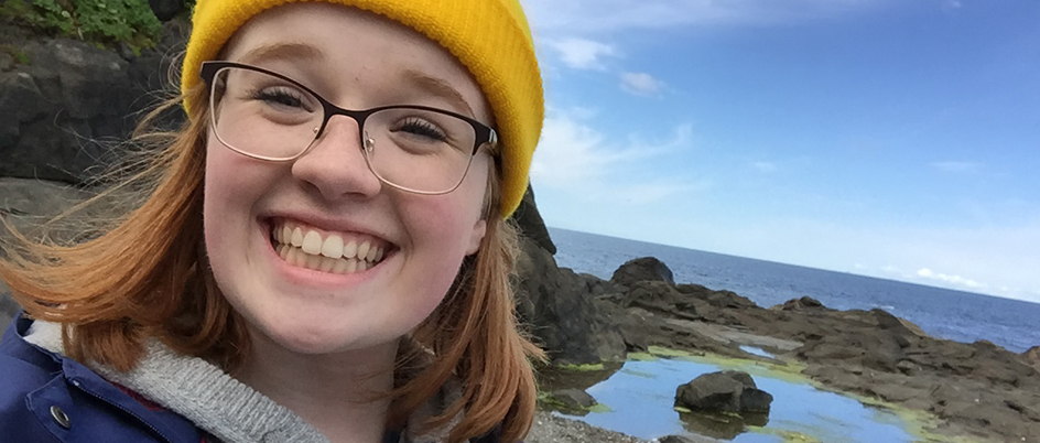 Undergraduate student Sydney Hunt smiles at camera with ocean in background