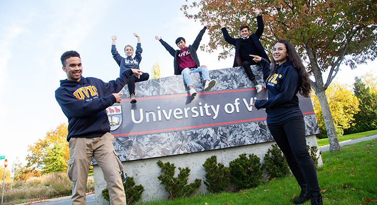 Students in front and sitting on top of UVic sign