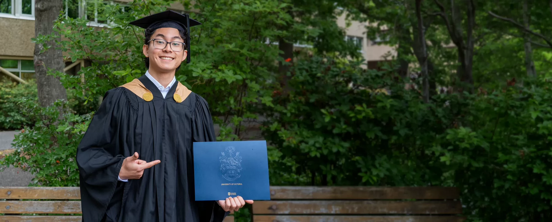 A new graduate smiling and holding a diploma..