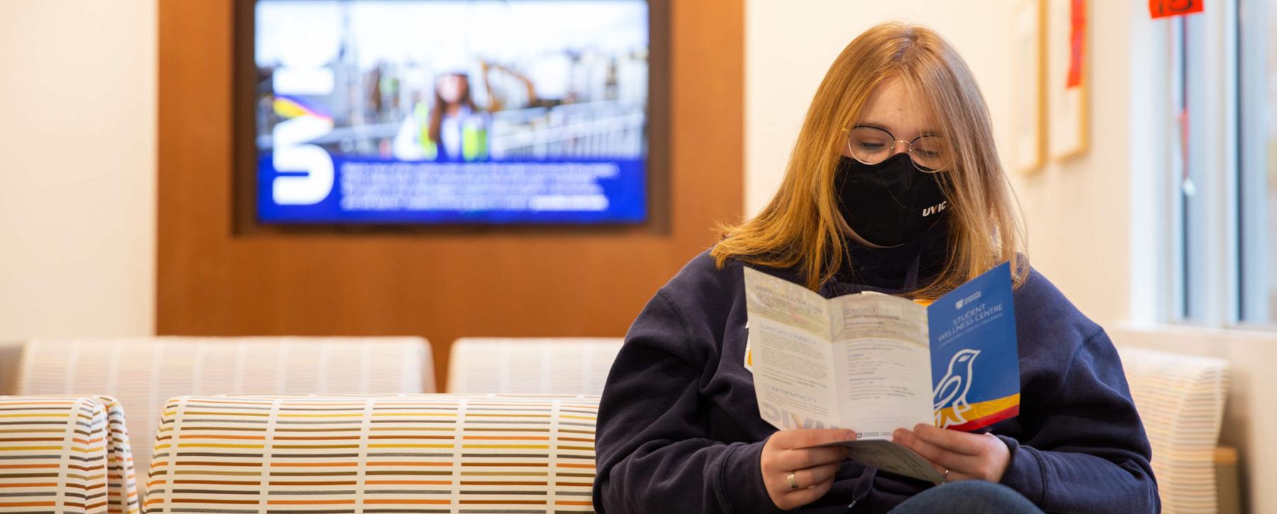 A masked student reads a pamphlet while seated at the UVic Student Wellness Centre.