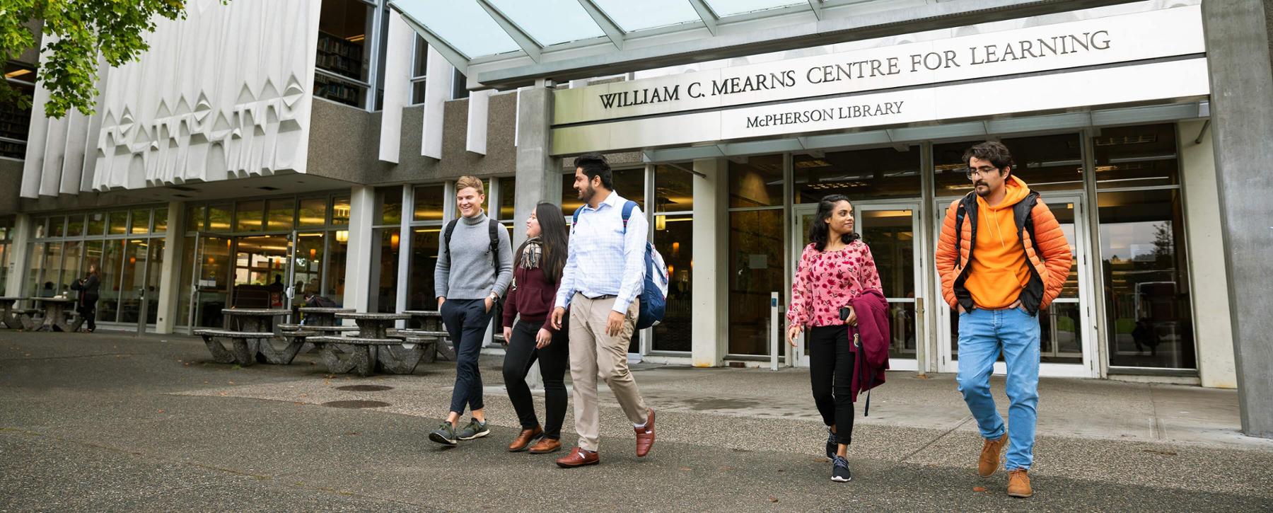 A group of five students walk away from the entrance of the Mearns Centre at UVic campus.