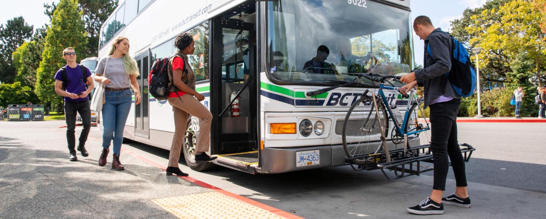 Students board a BC transit bus while another student places their bike on the front rack.