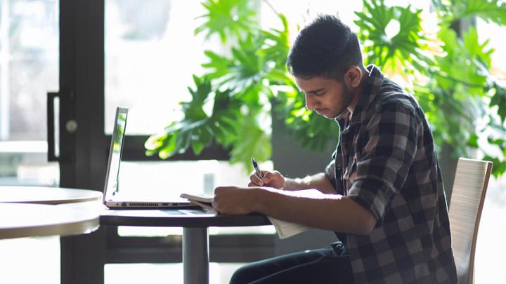male student studies at a table with lots of plants around him