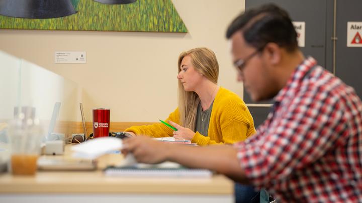 Woman sits looking at a computer with man studying in foreground