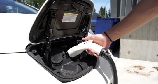 Close up shot of a hand plugging an electric vehicle charger into the charging port on the hood of the vehicle.