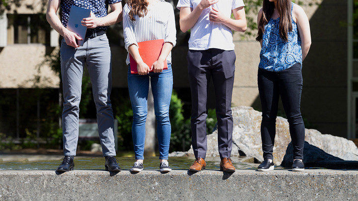 the legs of four people standing on the edge of a fountain