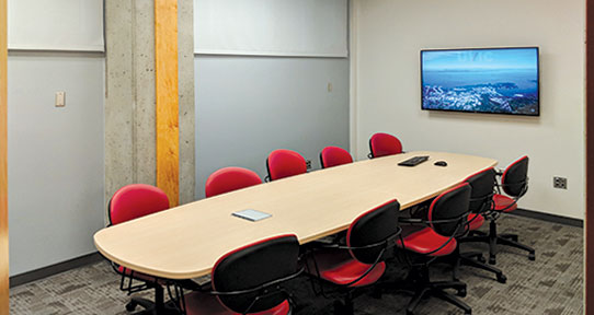 Interior of BEC 188. There's a long conference table, 10 office chairs, and a large-screen display on the wall.