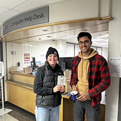 CyberAware 2022 winner. Two people standing in front of the Computer Help Desk holding the gift card and mug prize