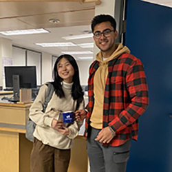 CyberAware 2022 winner. Two people standing in front of the Computer Help Desk holding the gift card and mug prize