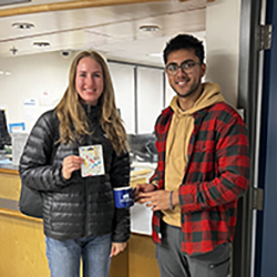 CyberAware 2022 winner. Two people standing in front of the Computer Help Desk holding the gift card and mug prize