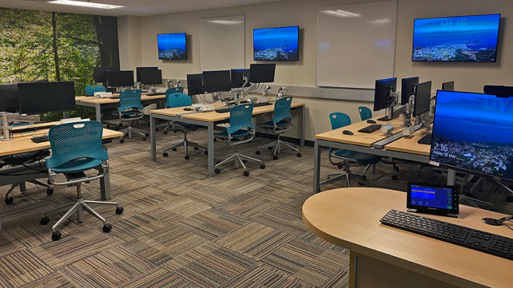 Small classroom with rows of computer desks, some facing away from instructor station.