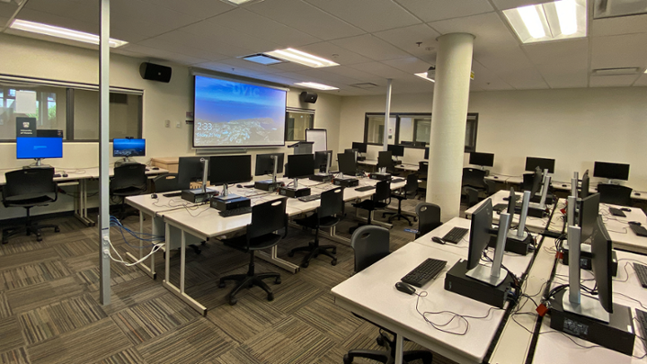 Classroom with rows of computer desks, some facing away from instructor station.