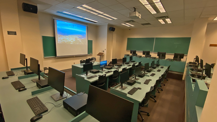 Classroom with rows of computer desks facing instructor station, room has different floor levels.