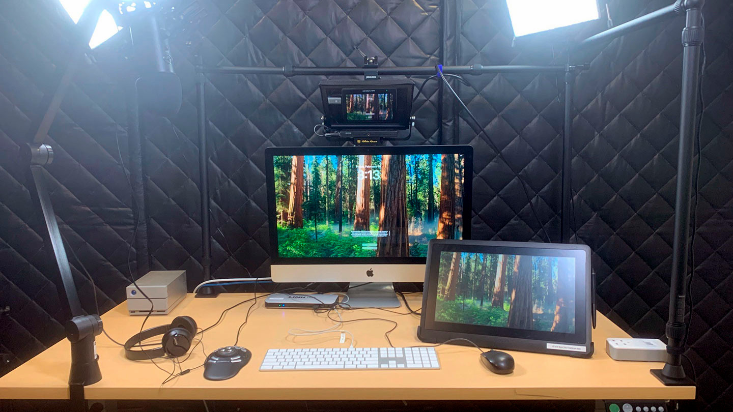 An iMac with media accessories on an electric height-adjustable desk. There are video lights, a Wacom creative display, headphones, Blue Yeti mic, a camera and teleprompter.