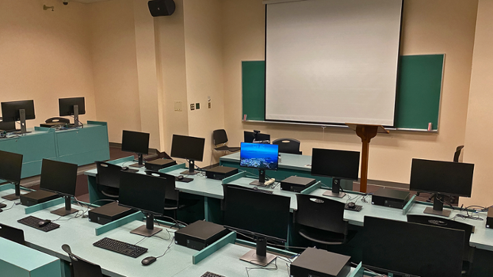 Classroom with rows of computer desks facing instructor station, room has different floor levels.