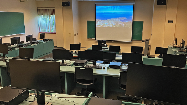 Classroom with rows of computer desks facing instructor station, room has different floor levels.