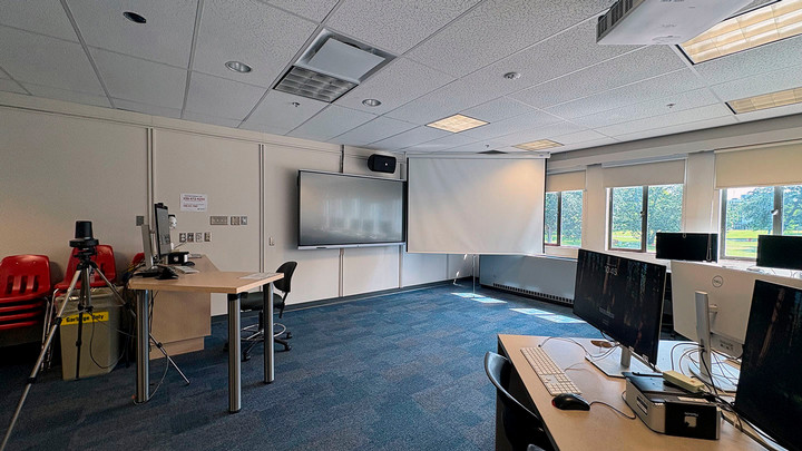 Photo from the back of the classroom showing the projector screen, smart display, and instructor station