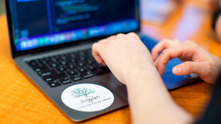 Hands working on a laptop with the INSPIRE logo visible.