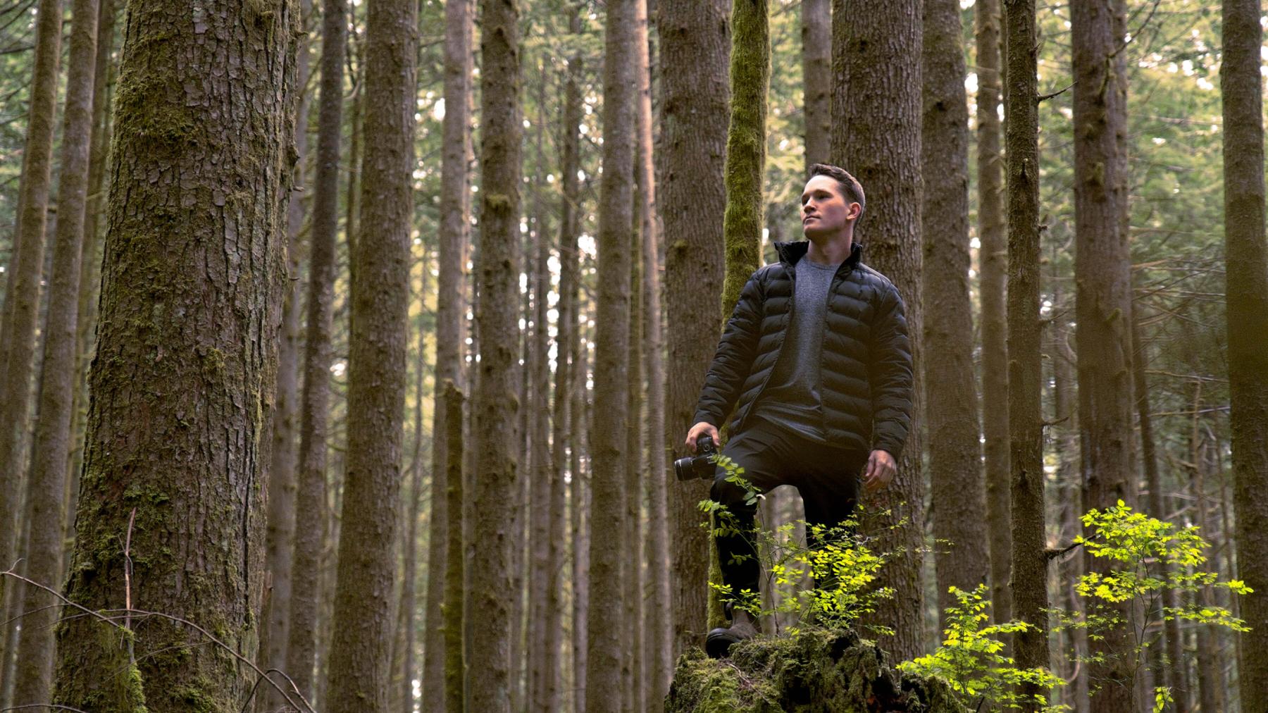 Griffin Young stands in the forest, holding a camera to document wind severity and help classify storms.
