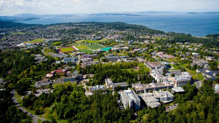 aerial photo showing campus on land next to ocean, with mountains on the horizon