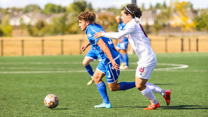 Harry Ritter-West running down a soccer field with a ball being checked by an opposing player.