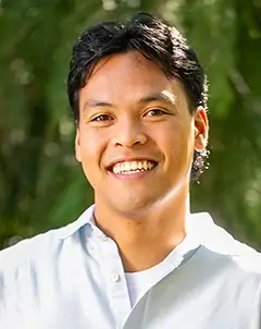 Person with short curly dark hair wearing a dark grey knit sweater, smiling at the camera.