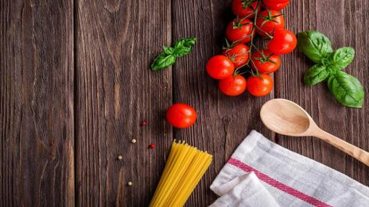 Spaghetti noodles, fresh tomatoes and basil on a wooden table.