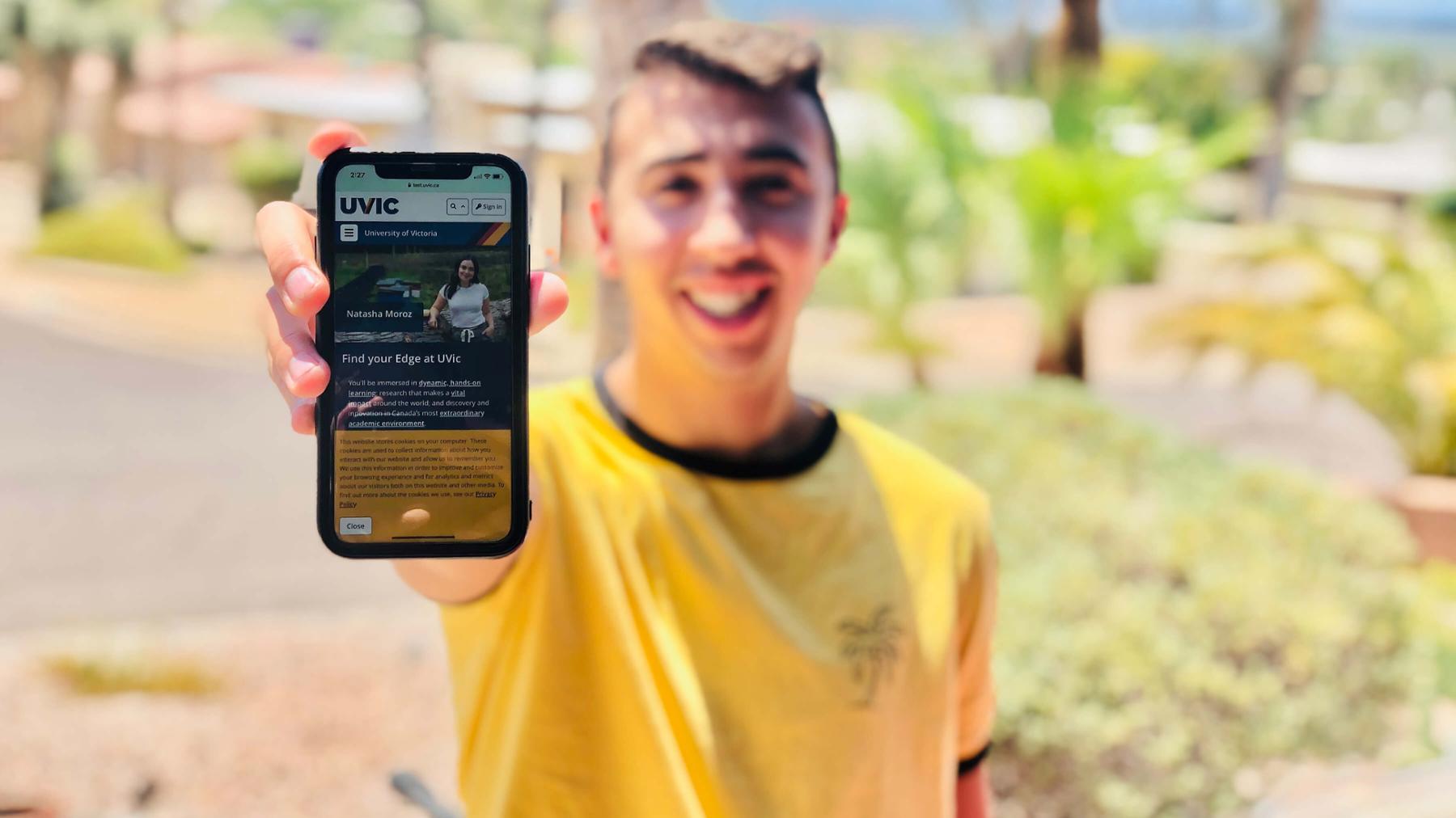 A student holds up a smartphone to the showing the new UVic website on its screen.
